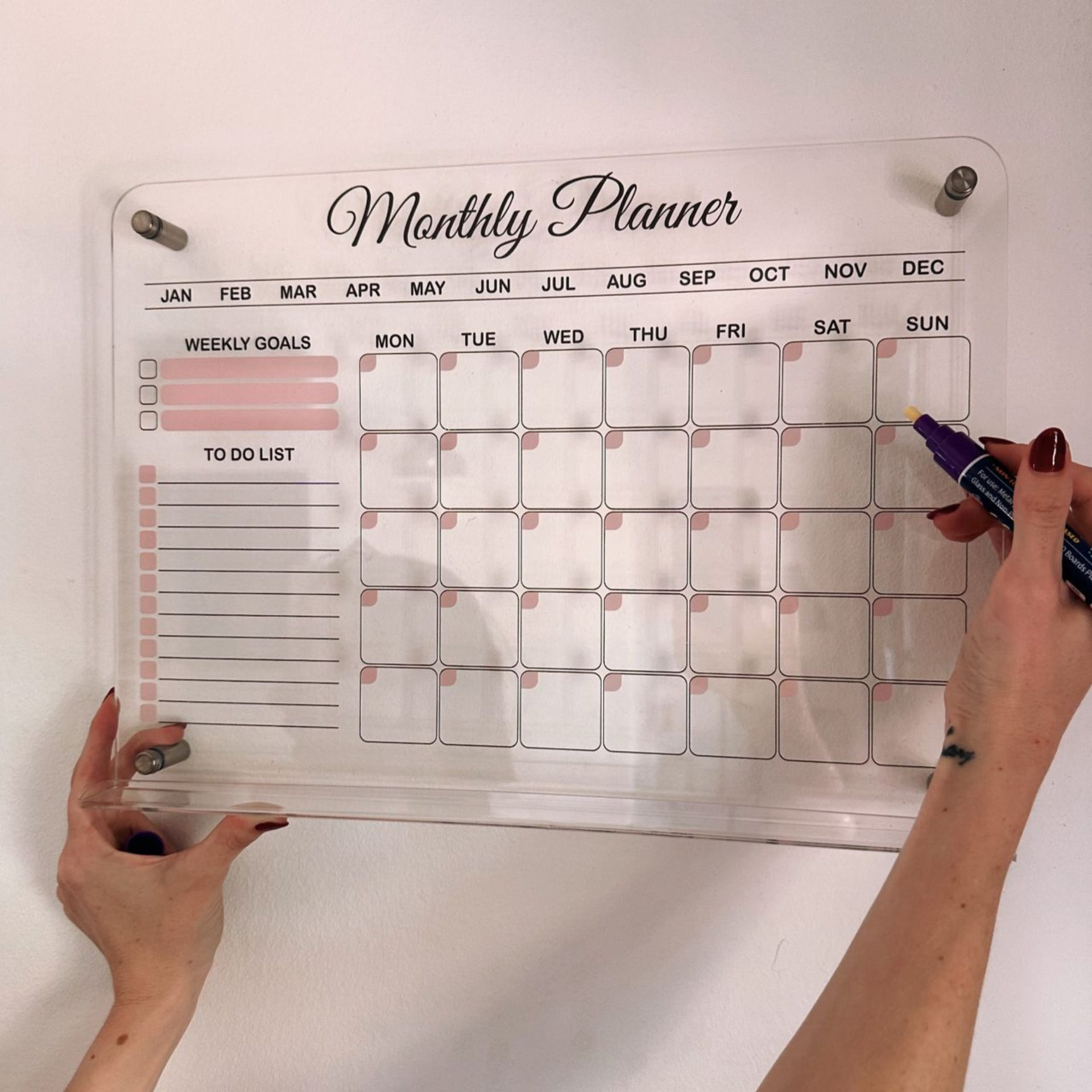 Clear acrylic monthly planner with pink accents being written on