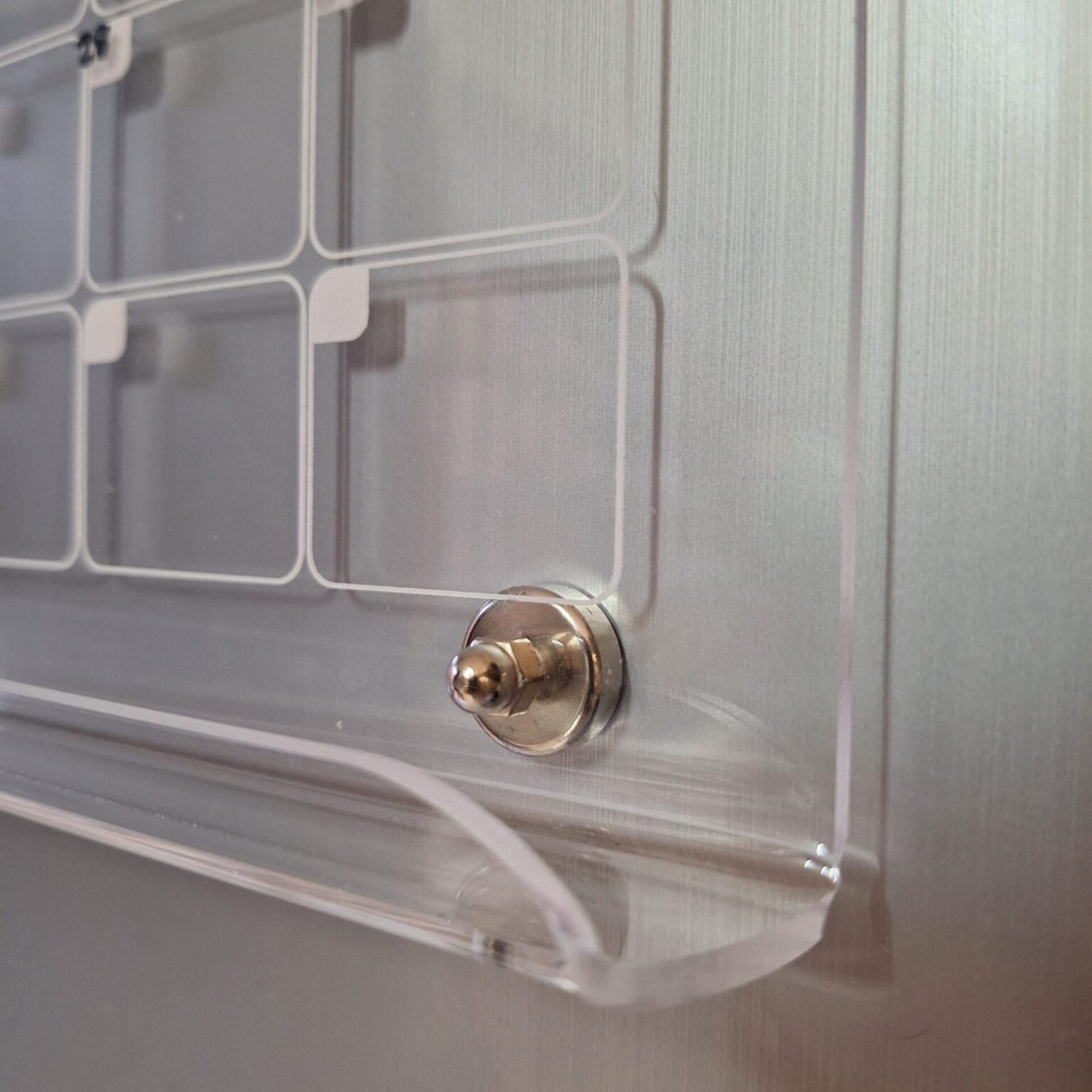 Close-up of a silver stand-off pin and acrylic pen ledge