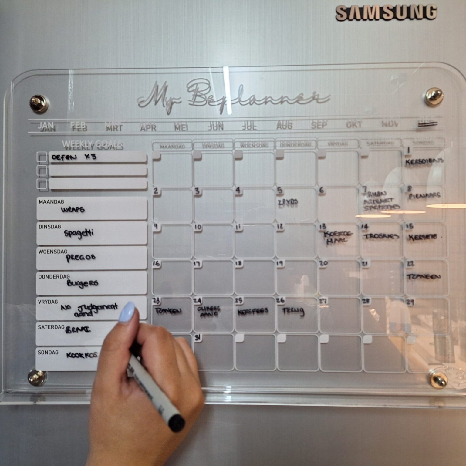 Afrikaans monthly planner in use on a fridge with gold pins